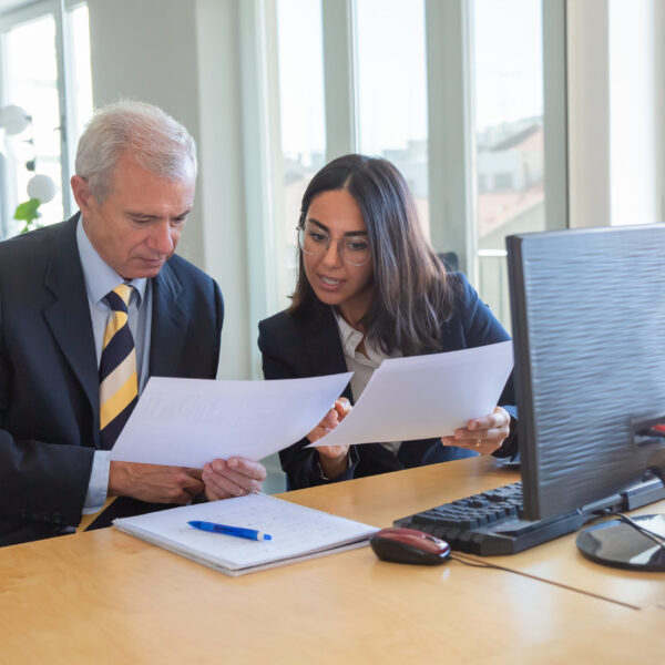 Female professional explaining document details to client at workplace. Serious business leader consulting financial or legal expert. Teamwork or cooperation concept